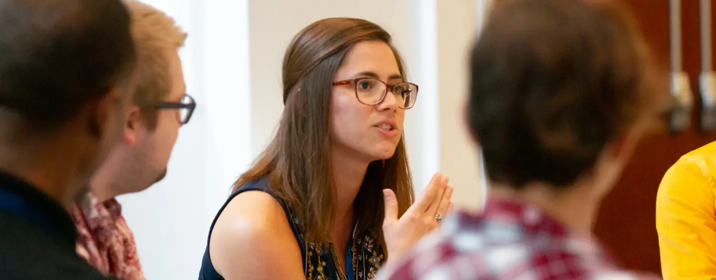 A woman in brown rimmed glasses speaking to other students while gesturing with her hands