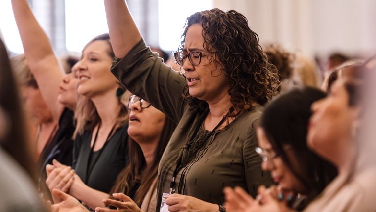 A group of women singing with arms raised