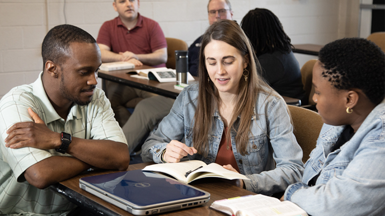 Students sitting around a desk looking at a book.