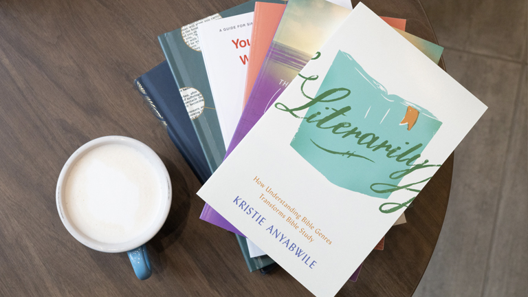 A stack of books and a cup of coffee on a brown table.