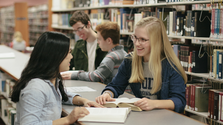 Students smiling and talking in the library.